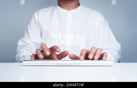 Businessman's hands in white shirt typing on modern keyboard computer on a white clean desk while working in front of the screen, front view, minimal Stock Photo