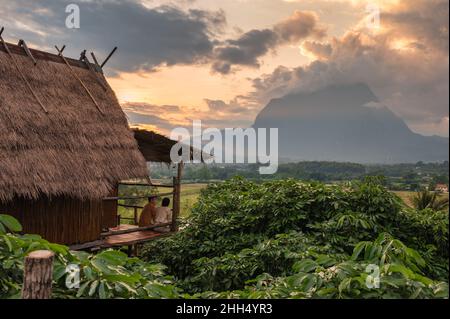 Young tourist couple sitting on balcony of wooden hut and sunset over Doi Luang Chiang Dao mountain at Chiang Dao, Chiang Mai, Thailand Stock Photo