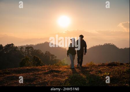 Silhouette young asian couple embracing enjoying on hill in countryside at sunset Stock Photo