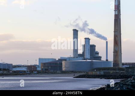 Poolbeg electricity generating station in Dublin bay, smoke blows into sky, people on beach. Dublin, Ireland Stock Photo