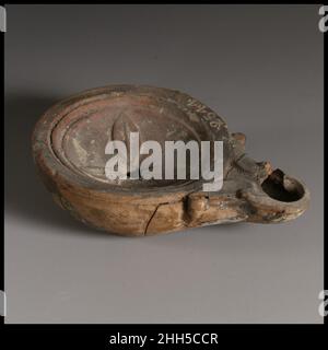 Terracotta oil lamp ca. A.D. 40–100 Roman Loeschcke Type 4. Mold-made. Deep concave discus: rosette of three pointed petals with central rib; a single filling hole at center; band of two grooves towards edge. Volutes flanking nozzle, with large wick hole. Incised base ring, and raised, flat base; a short impressed line near center.Broken and repaired, with some cracks, holes, and one chip missing on right side of nozzle.. Terracotta oil lamp  241459 Stock Photo