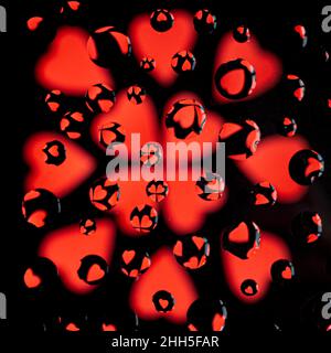 Red hearts on a black background behind glass with raindrops Stock Photo