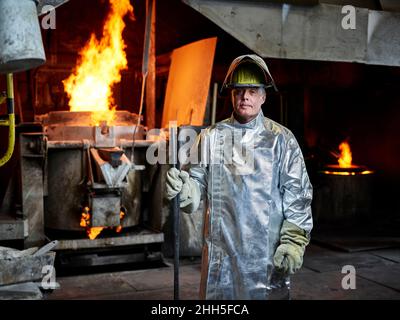 Metal worker wearing protective workwear standing with pipe in industry Stock Photo