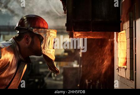 Blue-collar worker wearing protective helmet looking at burning furnace in industry Stock Photo