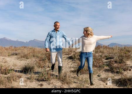 Cheerful couple holding hands running at dunes Stock Photo