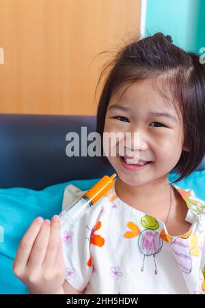 Close up of illness asian child smiling happily while admitted in hospital, taking medicine syrup. Girl feeling happy and looking at camera, facial ex Stock Photo