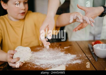 Mother helping son to knead dough on table Stock Photo