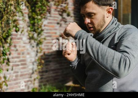 Young man practicing punching by ivy wall Stock Photo