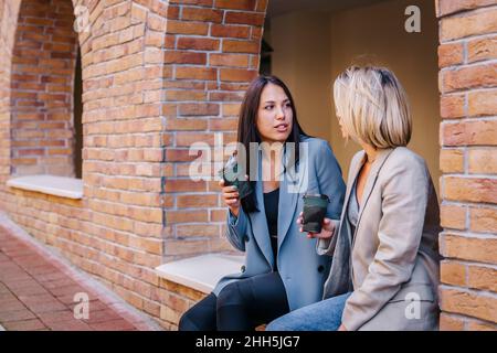 Friends with disposable coffee cups having serious conversation Stock Photo