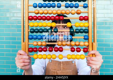 Young woman holding multi colored abacus in front of brick wall Stock Photo