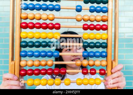 Thoughtful woman with multi colored abacus in front of brick wall Stock Photo