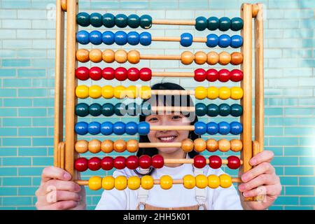 Smiling young woman holding abacus in front of brick wall Stock Photo