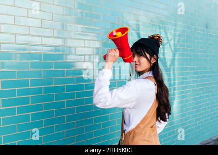 Young woman holding megaphone standing in front of turquoise wall Stock Photo