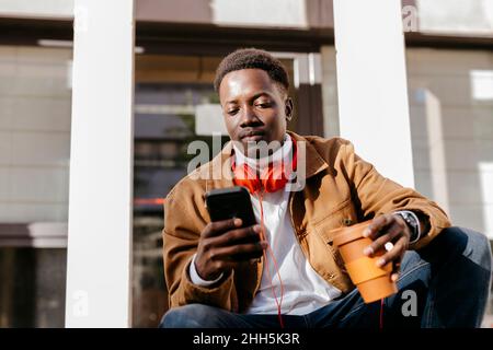 Young man holding reusable cup using smart phone Stock Photo