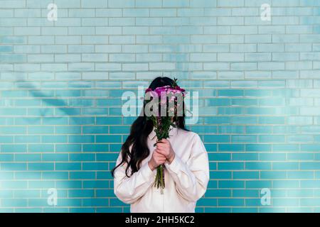 Young woman hiding face behind bouquet in front of brick wall Stock Photo