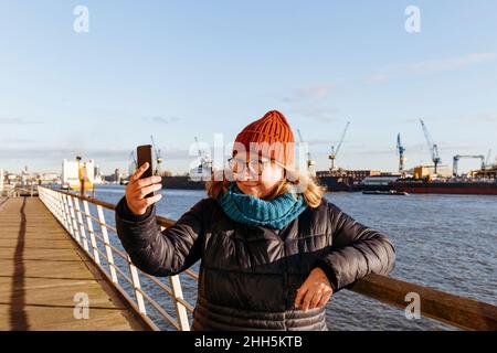 Senior woman taking selfie through smart phone at harbor Stock Photo