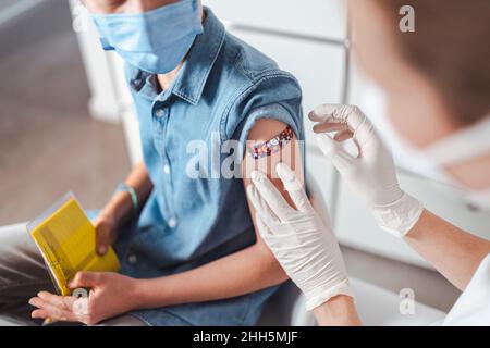 Healthcare worker putting adhesive note on vaccinated boy's arm at center Stock Photo