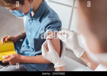 Nurse putting adhesive bandage on boy's arm at vaccination center Stock Photo