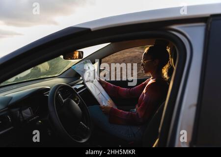 Young woman checking map in car at sunset Stock Photo