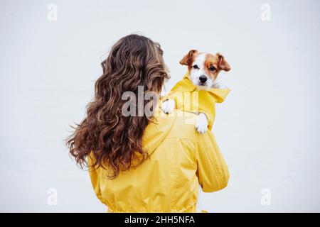 Woman with long brown hair carrying dog in front of white wall Stock Photo