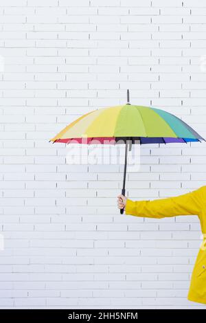 Woman holding multi colored umbrella in front of brick wall Stock Photo