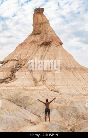 Man standing with arms outstretched in front of eroded mountain, Bardenas Reales, Navarra, Spain Stock Photo