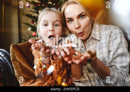 Mother with daughter blowing confetti at home Stock Photo