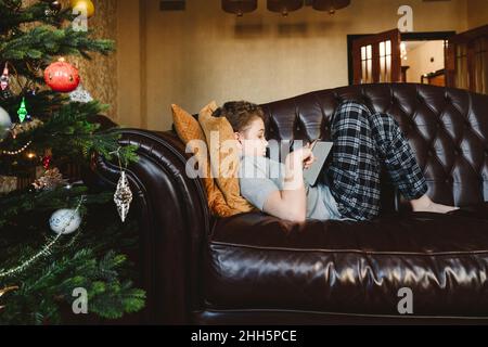 Boy using tablet PC lying on sofa at home Stock Photo