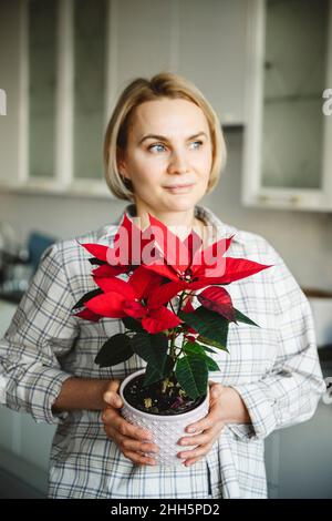 Thoughtful woman holding poinsettia plant at home Stock Photo