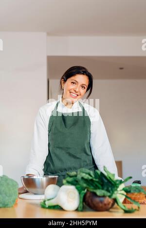 Smiling chef wearing apron standing at table with vegetables Stock Photo