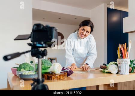 Smiling chef rolling dough making tutorial on digital camera at home Stock Photo