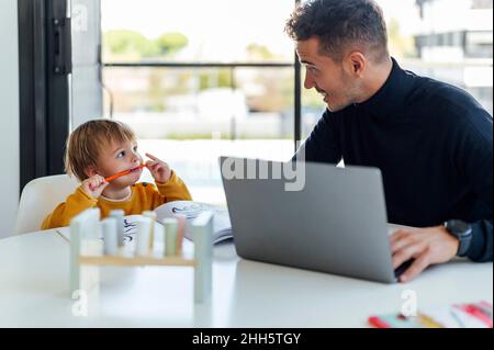 Father talking with son and working on laptop at home Stock Photo