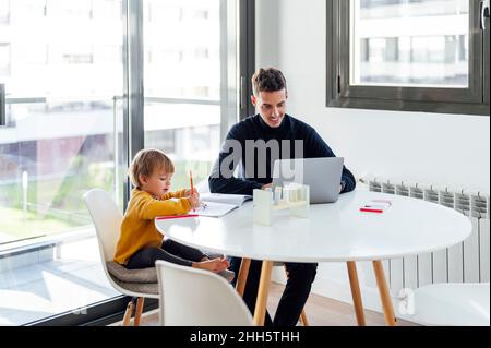 Son drawing by father freelancing on laptop at table Stock Photo