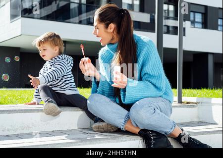 Cheerful mother and son playing with soap bubbles on sunny day Stock Photo
