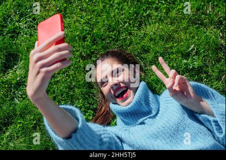 Cheerful woman taking selfie lying down on grass Stock Photo