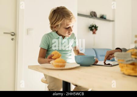 Boy using tablet PC and having cupcake at home Stock Photo