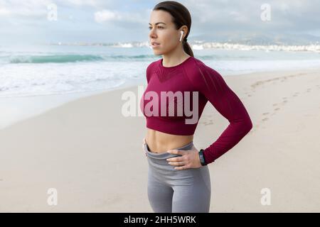 Fit woman standing with hands on hips at beach Stock Photo