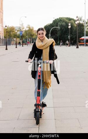 Happy teenager riding electric push scooter on footpath Stock Photo