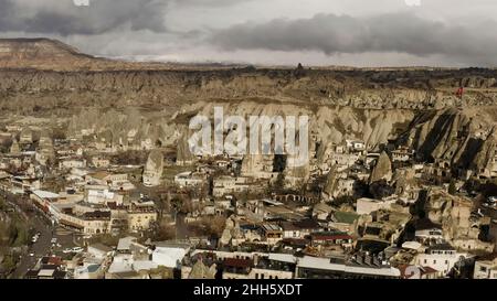 Aerial view of a small town located by the mountain range. Action. Red turkish flag waving on a rock top, sunny village in dry area Stock Photo