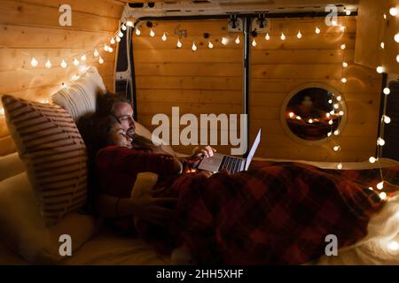 Young couple using laptop lying on bed in motor home Stock Photo