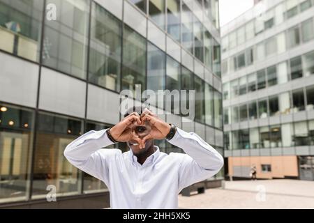 Young man making heart shape in front of building Stock Photo