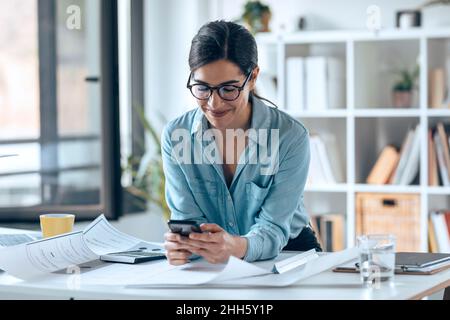 Smiling businesswoman using smart phone in small office Stock Photo