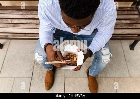 Young man having food sitting on bench Stock Photo