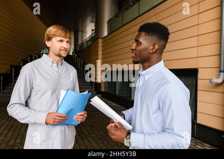Friends with documents talking on footpath Stock Photo
