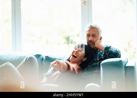 Cheerful woman pointing sitting with man in living room Stock Photo