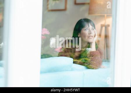 Thoughtful woman looking through window Stock Photo