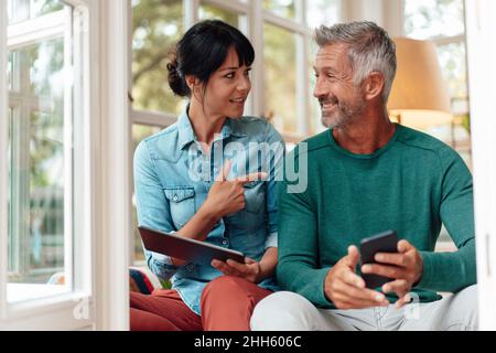 Woman holding tablet PC talking with smiling man at home Stock Photo