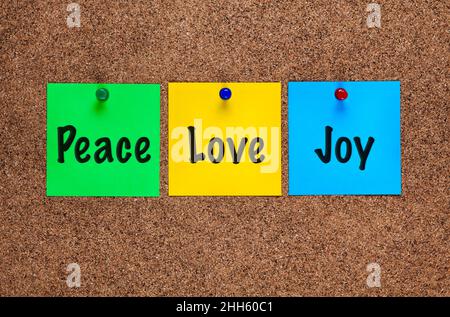 Three colored notes on a corkboard with words Peace, Love, Joy. Stock Photo