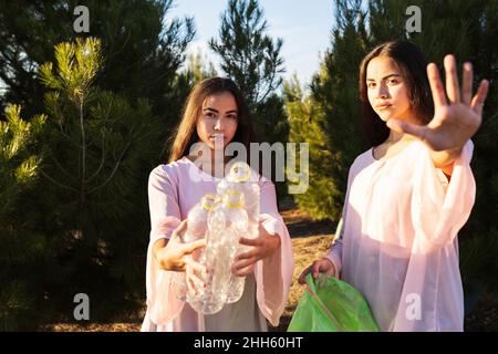 Angry woman making stop gesture standing by sister with empty plastic bottles in forest Stock Photo