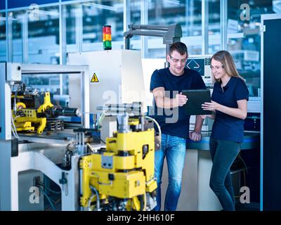 Smiling engineers discussing on tablet PC in automated factory Stock Photo